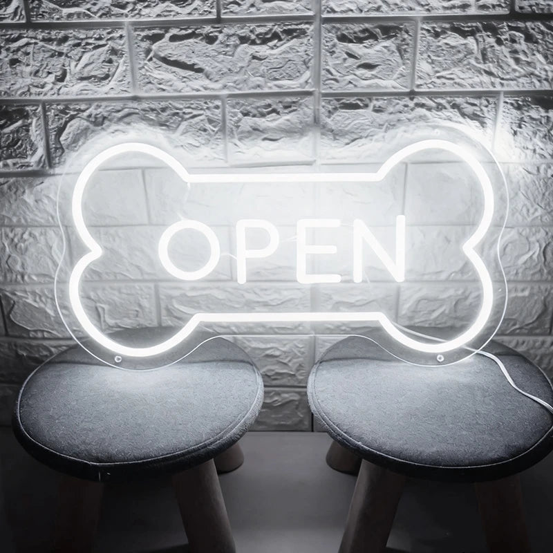 White neon sign shaped like a bone with 'OPEN' text on a textured wall background.