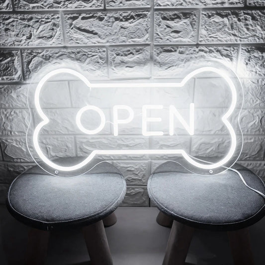 White neon sign shaped like a bone with 'OPEN' text on a textured wall background.