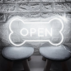 White neon sign shaped like a bone with 'OPEN' text on a textured wall background.