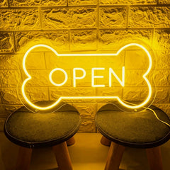 Lemon yellow neon sign shaped like a bone with 'OPEN' text on a textured wall background.