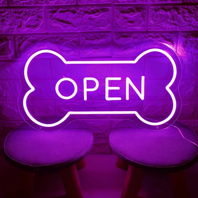 Purple neon sign shaped like a bone with 'OPEN' text on a textured wall background.
