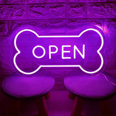 Purple neon sign shaped like a bone with 'OPEN' text on a textured wall background.