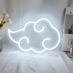 Neon cloud-shaped sign on a white surface with a vase of flowers and books in the background.