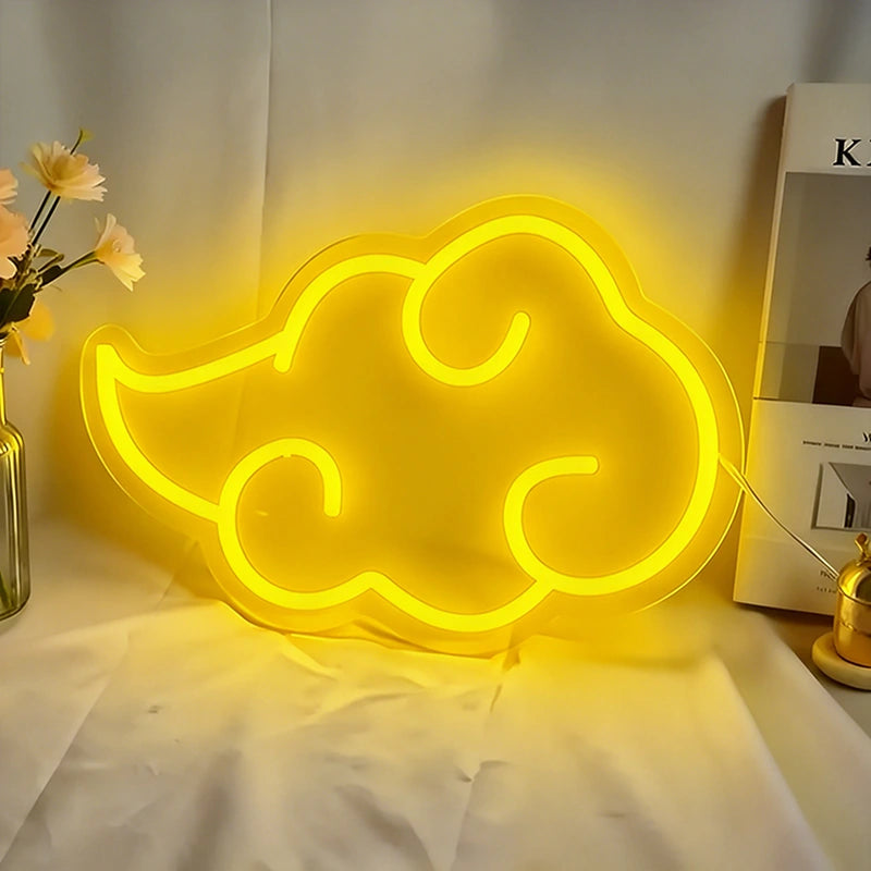 Yellow neon cloud-shaped sign on a white surface with a vase of flowers and books in the background.
