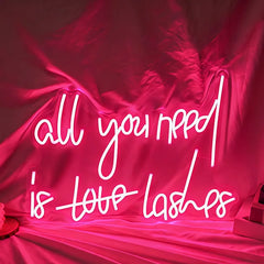 Neon sign with 'all you need is love lashes' text on a pink fabric background