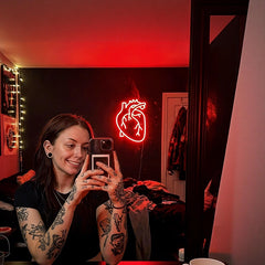 Person with tattoos using a phone in a room with a heart-shaped neon light.