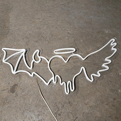Neon angel with demon heart-shaped sign on a concrete floor
