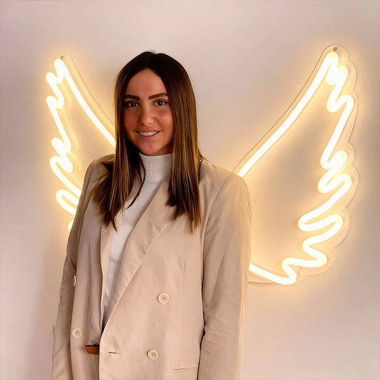 Woman standing in front of neon angel wings on a white wall