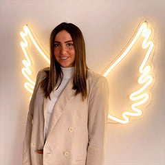 Woman standing in front of neon angel wings on a white wall