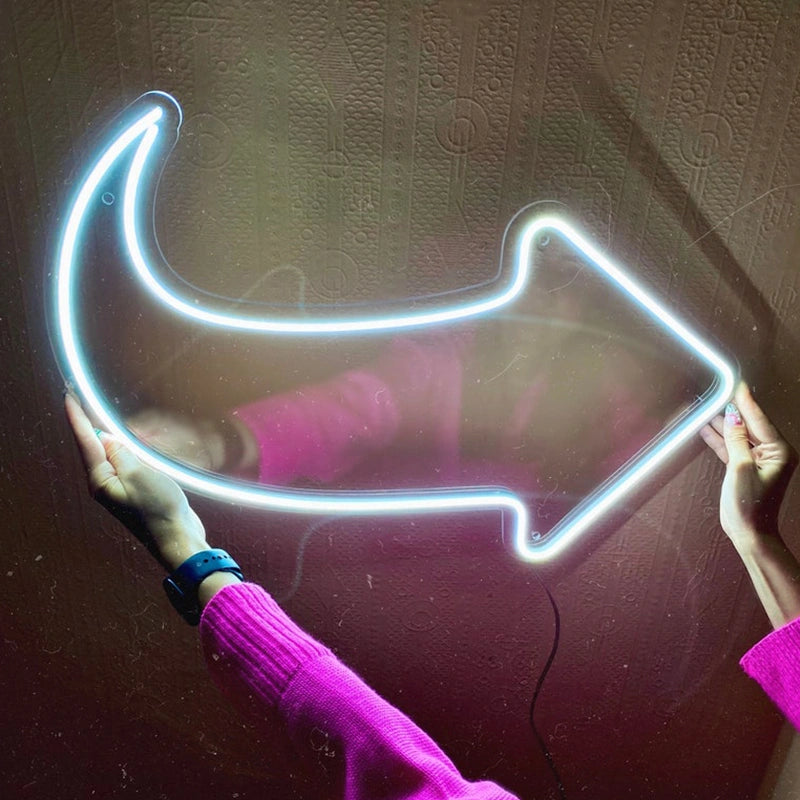 Neon arrow-shaped light held by a person wearing a pink sweater against a textured wall.