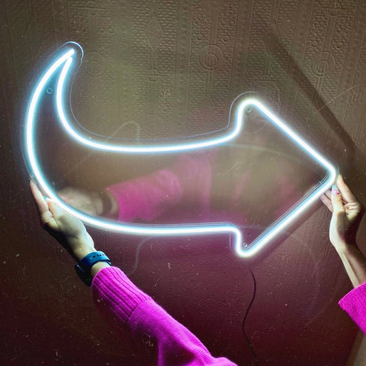 Neon arrow-shaped light held by a person wearing a pink sweater against a textured wall.