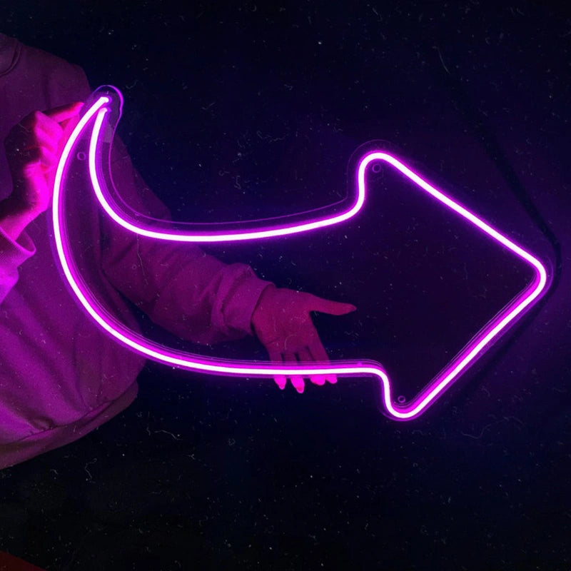 Person holding a hot pink neon arrow-shaped light against a dark background