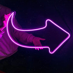 Person holding a hot pink neon arrow-shaped light against a dark background