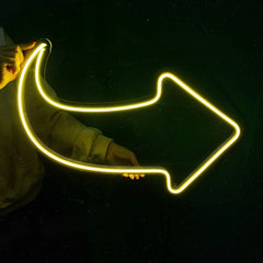 Person holding a neon lemon yellow arrow-shaped light against a dark background