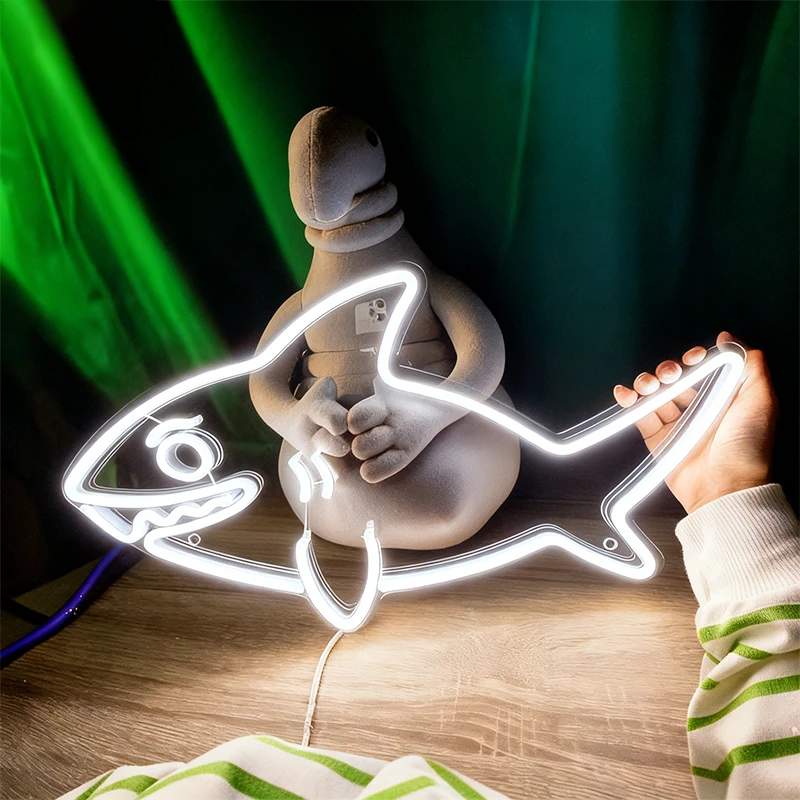 Neon white light shaped like a fish with a small figure inside, held by a person on a wooden surface.