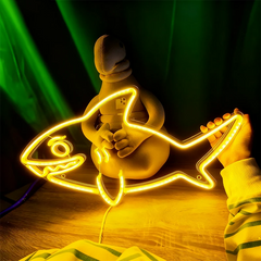 Neon lemon yellow light shaped like a fish with a person holding it, on a dark background