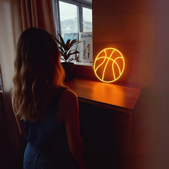 Person standing in a room with a neon basketball light on a table.