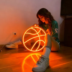 Person sitting on the floor with a glowing orange color basketball neon sign.