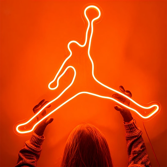 Neon Jordan logo with a person's silhouette reaching towards it on an orange background