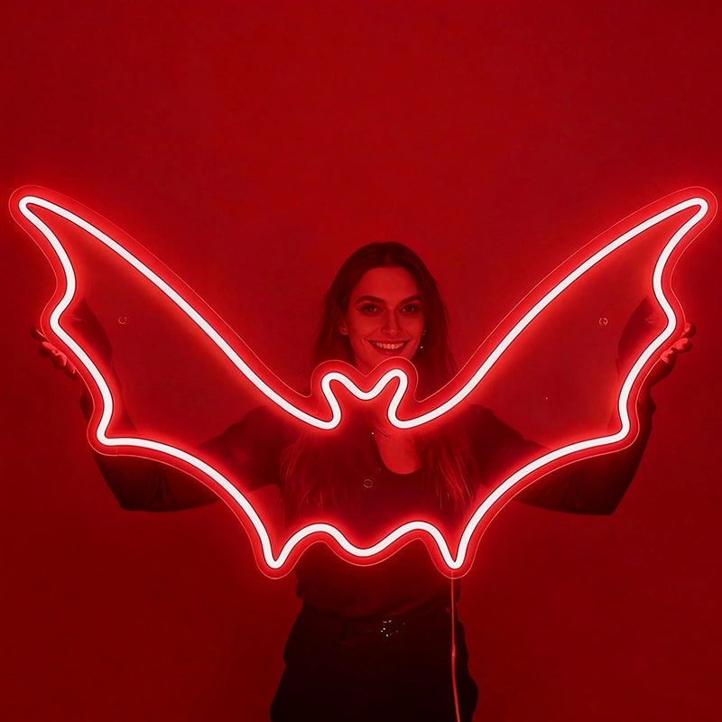 A smilling woman holding a red color neon sign shaped like a bat in a dark background.
