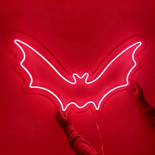 Person holding a red color neon sign shaped like a bat in a dark background.
