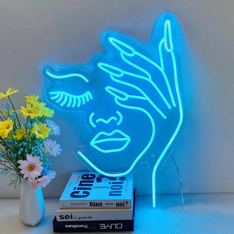 Neon blue light shaped like a beauty woman face with a hand on a surface with books and flowers.