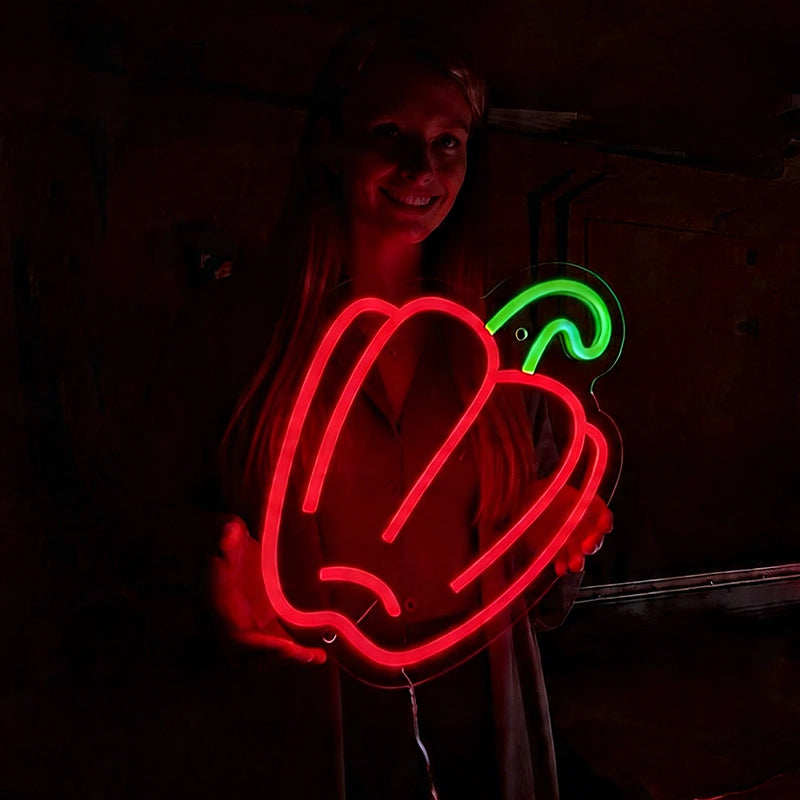 Person holding a red neon sign shaped like a bell pepper on a dark background