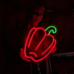 Person holding a red neon sign shaped like a bell pepper on a dark background