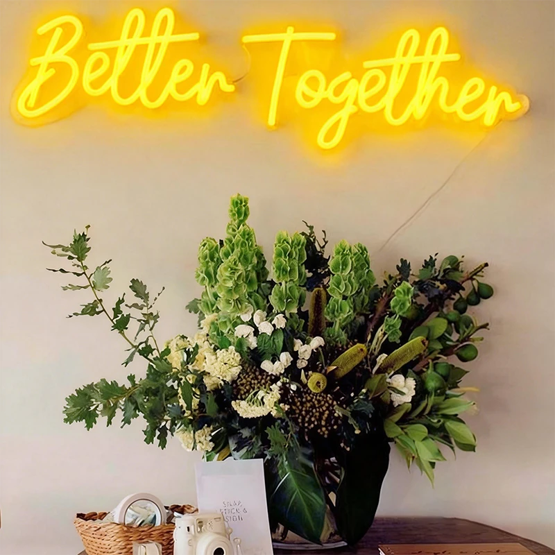 Neon sign with 'Better Together' text above a floral arrangement on a table.