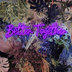 Neon sign with 'Better Together' surrounded by tropical plants and flowers