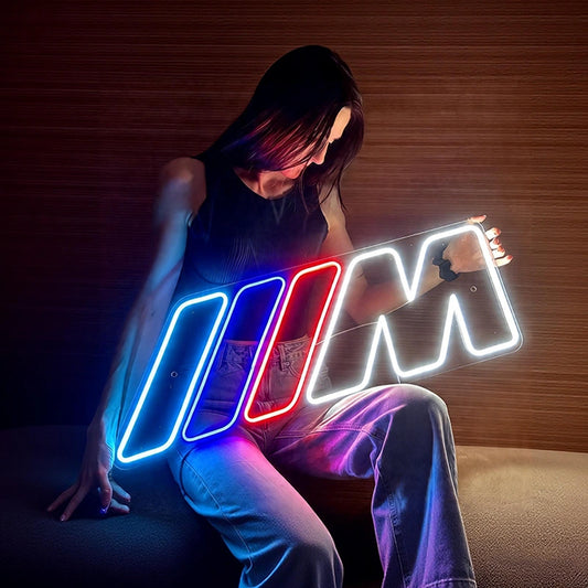 Person holding a bmw m power logo neon sign in a dimly lit room.
