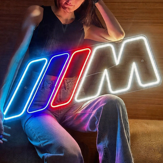 Person sitting next to a bmw m power logo neon sign on a wooden floor.