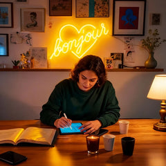 Person using a tablet at a desk with a 'bonjour' neon sign in the background