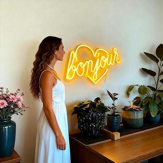 Neon sign with 'bonjour' in a heart shape on a wall with a person and plants in the foreground.