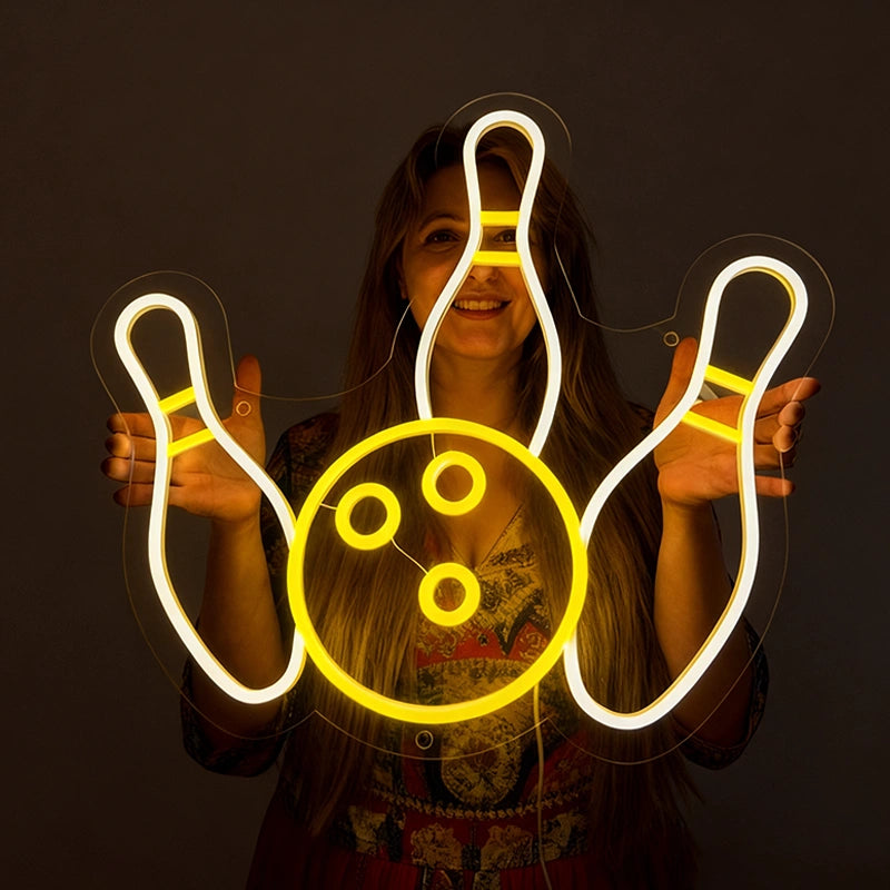 A smilling woman holding a neon sign shaped like bowling with lemon yellow and white color in a dark background