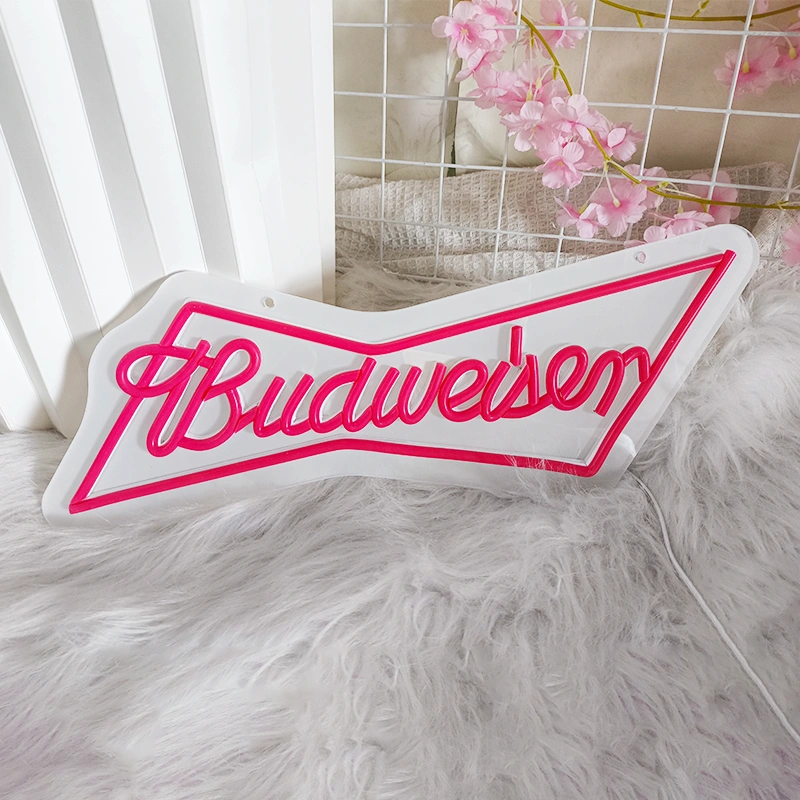 Budweiser logo neon sign on a fluffy surface with pink flowers in the background