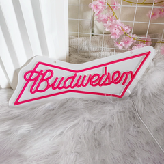 Budweiser logo neon sign on a fluffy surface with pink flowers in the background