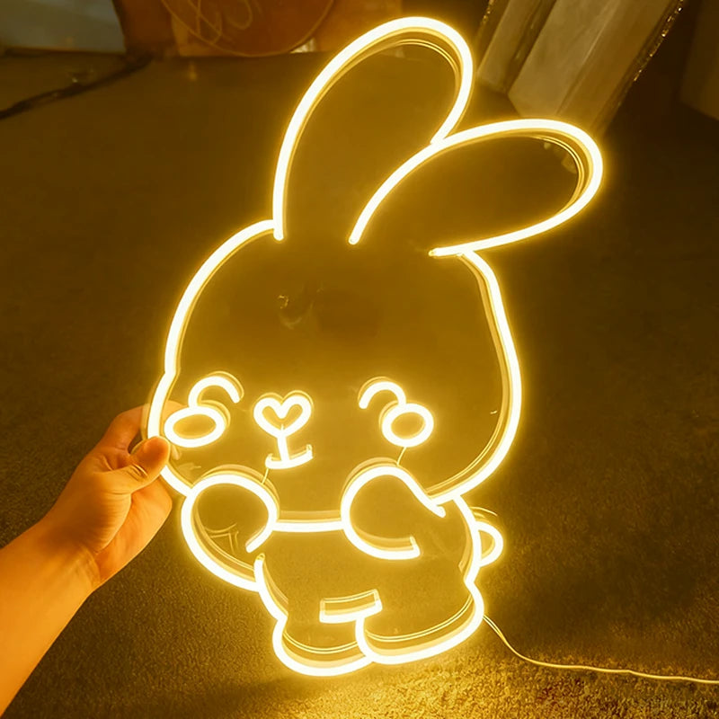 Neon warm white bunny light shaped like a cartoon character held by a hand on a dark surface.