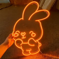 Neon light shaped like a cartoon rabbit held by a hand on a dark background