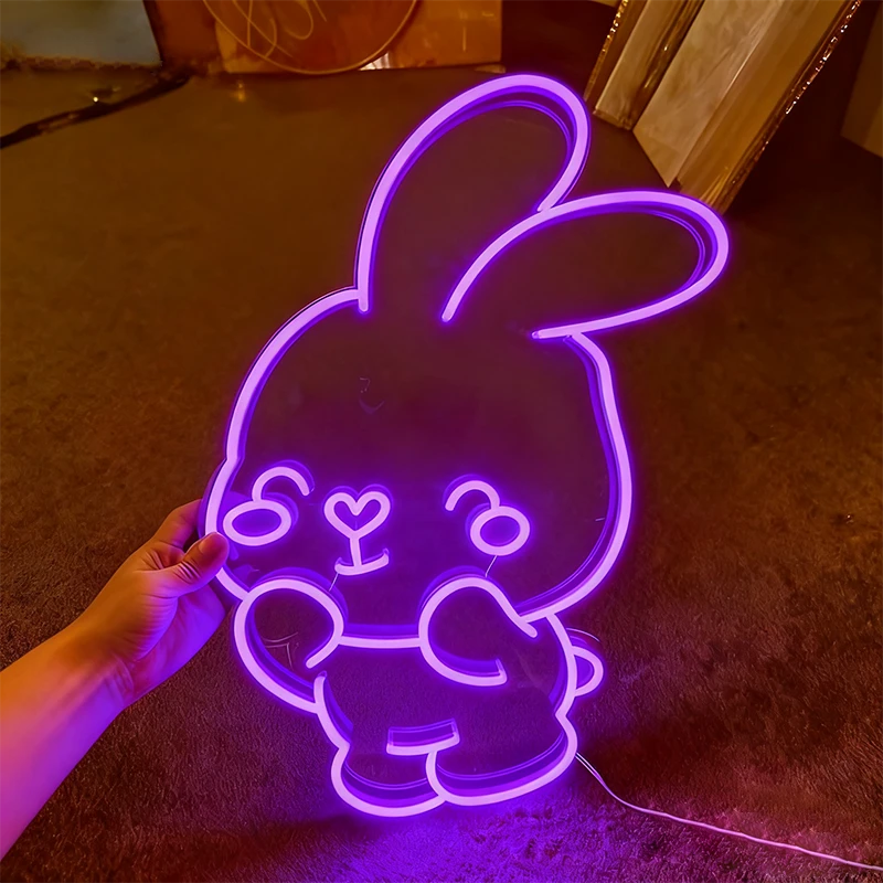 Neon light shaped like a cartoon bunny held by a hand on a dark surface.