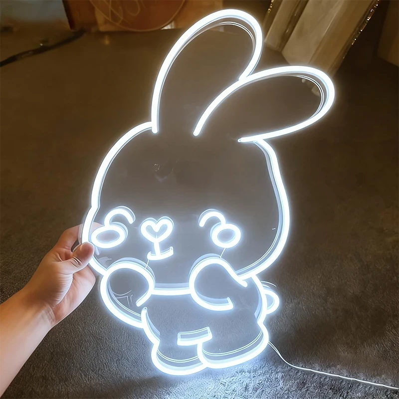 Neon white bunny light shaped like a cartoon character held by a hand on a dark surface.