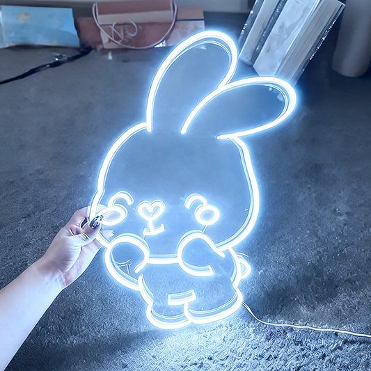 Neon white bunny light shaped like a cartoon character held by a hand on a dark surface.