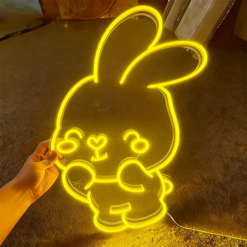 Neon yellow bunny light shaped like a cartoon character held by a hand on a dark surface.