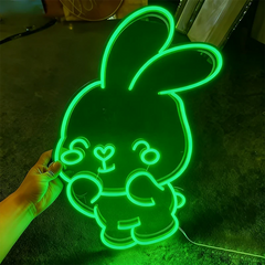 Neon green bunny-shaped sign with text held by a hand on a dark surface