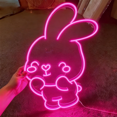 Neon pink bunny light shaped like a cartoon character held by a hand on a dark surface.
