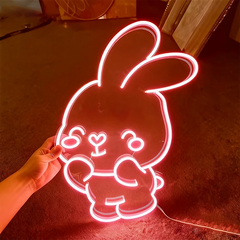 Neon light pink bunny light shaped like a cartoon character held by a hand on a dark surface.
