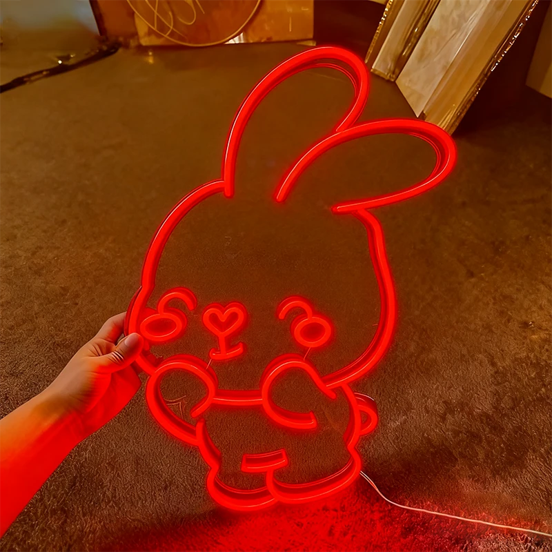 Red neon bunny light held by a hand on a brown floor.