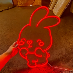 Red neon bunny light held by a hand on a brown floor.