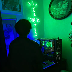 Bright green Cactus Jack neon sign mounted above a gaming PC setup, Travis Scott inspired LED wall art for gamer rooms, studios, and bedroom decor.