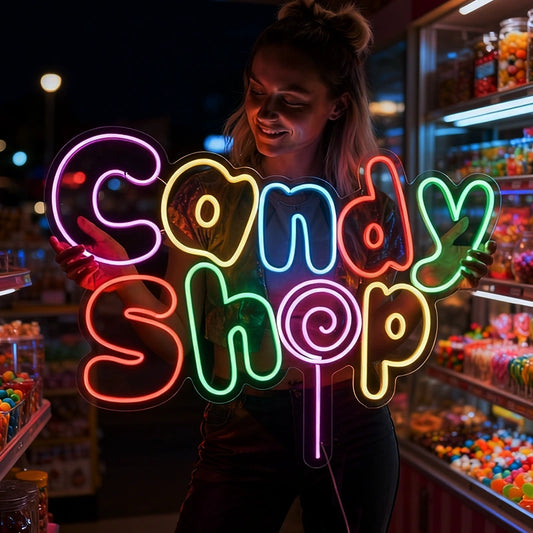 Person holding a colorful neon 'Candy Shop' sign in a candy store.